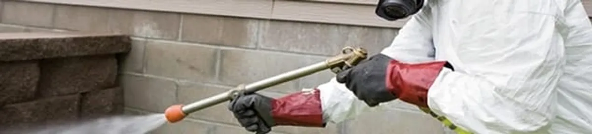 Pest control technician applying exterior insect treatment along a home foundation in Worcester, MA