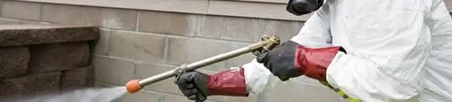 Pest control technician applying exterior insect treatment along a home foundation in Worcester, MA