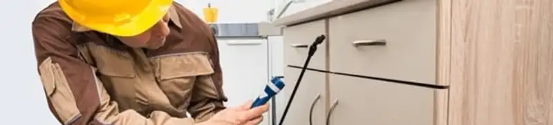 Roach exterminator applying treatment under kitchen cabinets in Worcester, MA