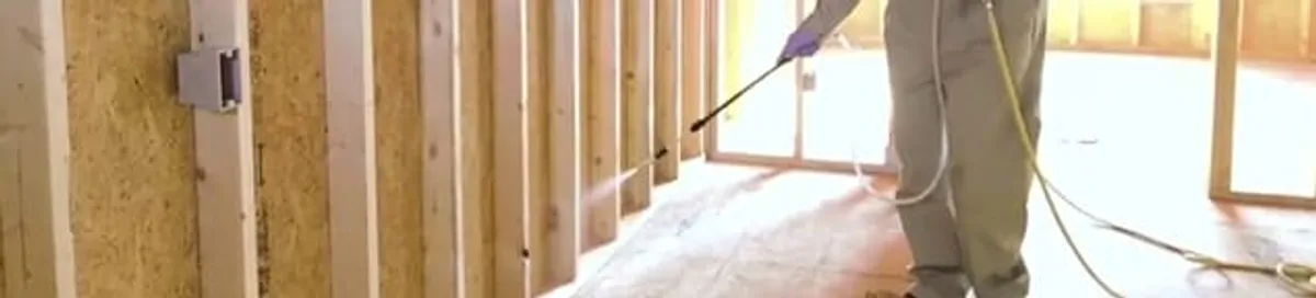 Termite treatment technician applying spray along framing and unfinished walls in Worcester, MA